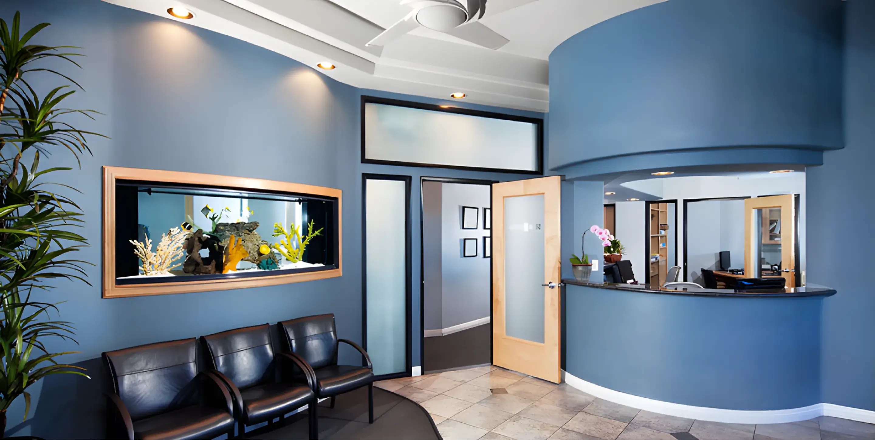 A dentist's office reception area with blue walls, fish tank, and seating chairs.