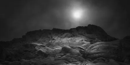 Rocky hill under a cloudy sky with the sun shining dimly above.