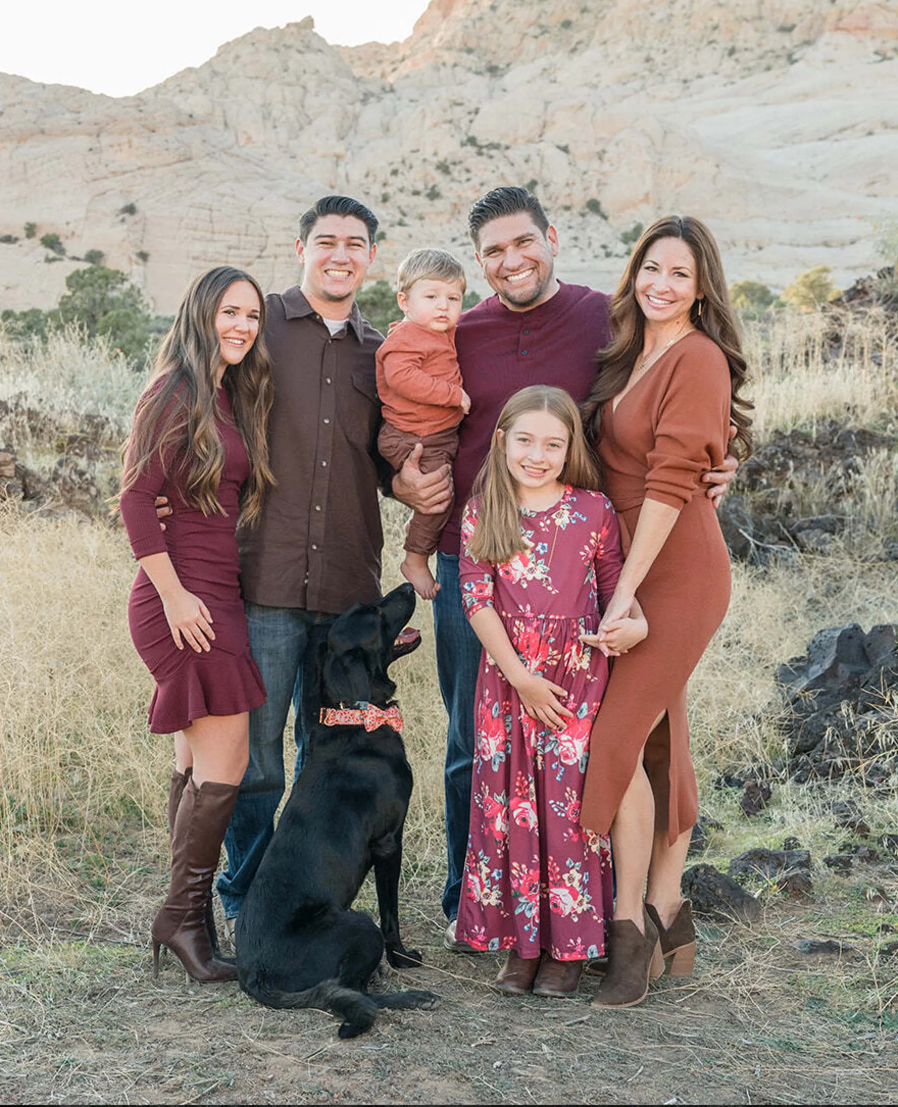 A group of six people and a black dog pose for a photo in an outdoor setting.